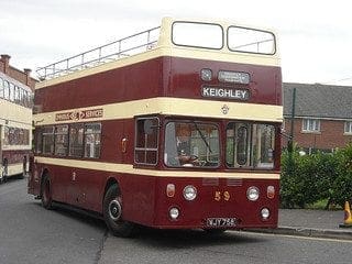 A maroon and cream double-decker bus marked Keighley, open top, number 59, is parked near homes—clearly distinguished features.