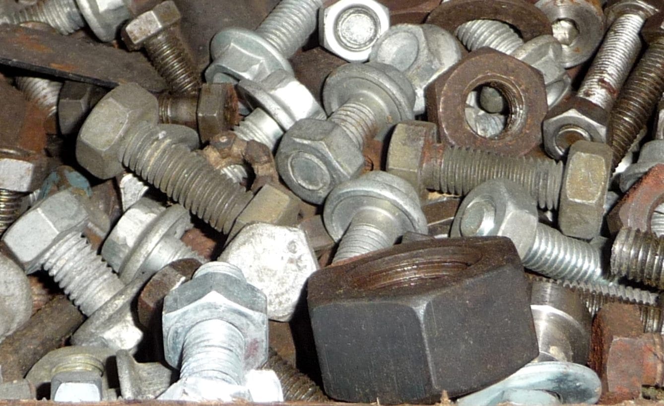 A close-up of mixed bolts and nuts, both new and worn, illustrating the real-world complexity of Buy-Side and Sell-Side Cyber Risk.