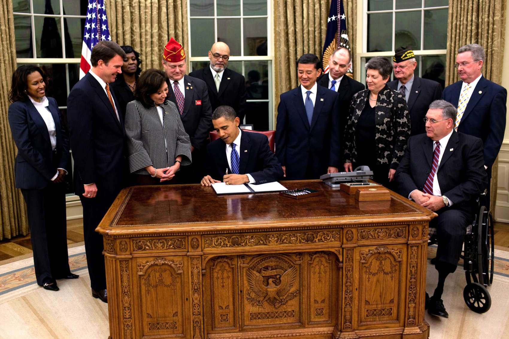 President Obama signs a key document at the Resolute Desk as officials and veterans look on, emphasizing sound cyber risk governance.