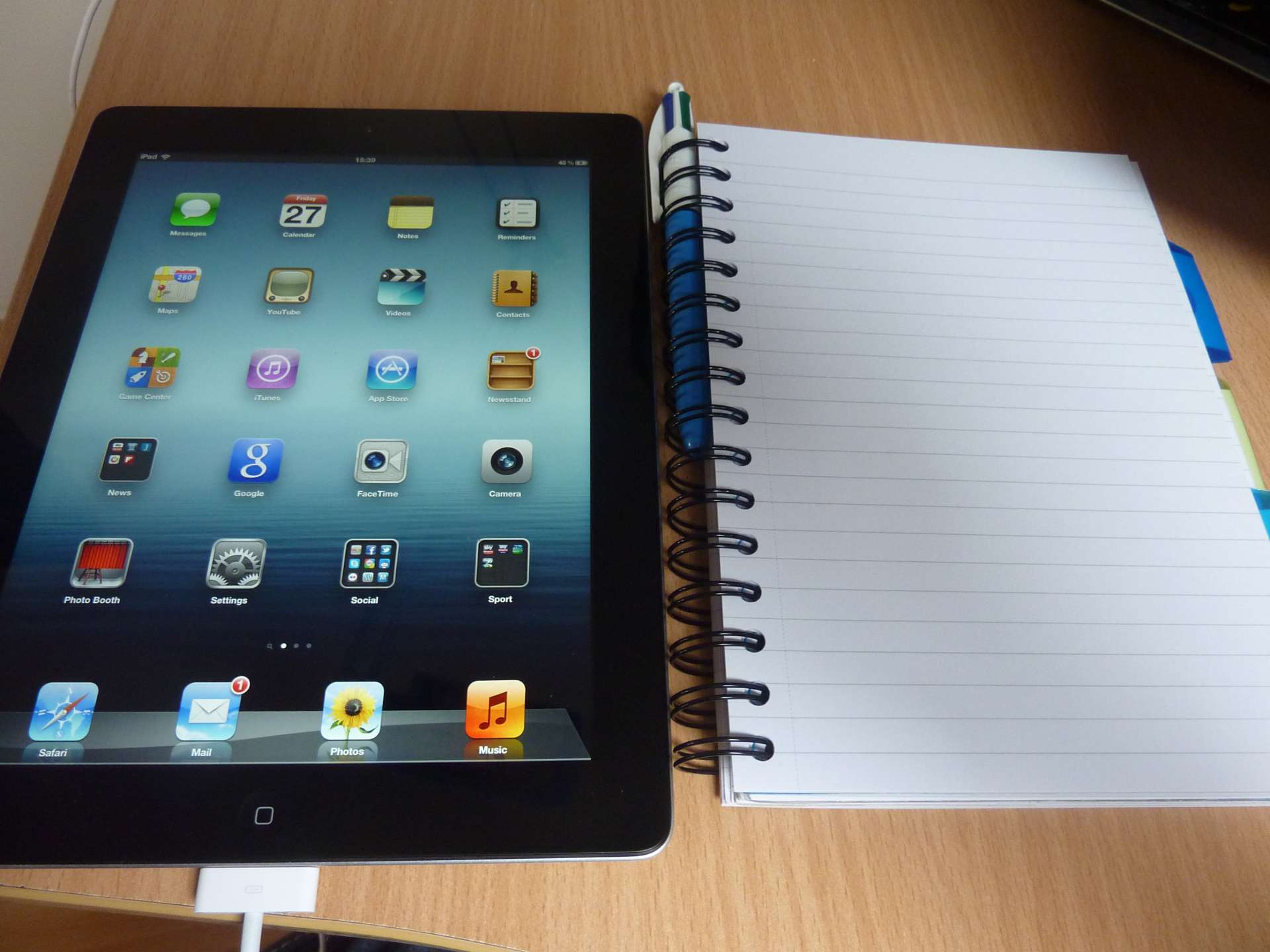 A black tablet with app icons rests on a wood desk beside an open notebook and blue pen—practical tools for cyber risk diligence.