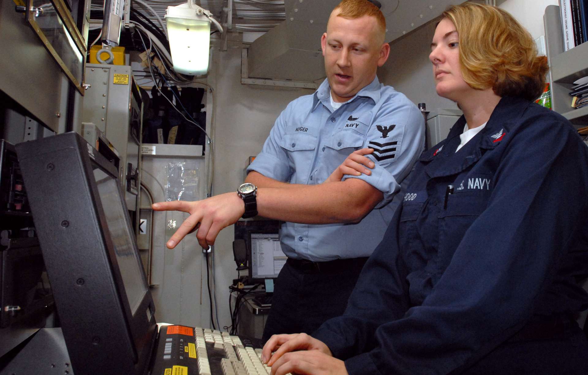 Two U.S. Navy personnel review a monitor at a shared station, collaboratively analyzing Buy-Side and Sell-Side Cyber Risk data.