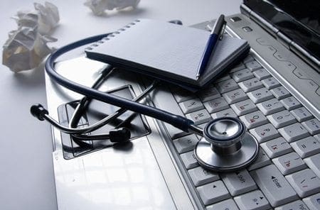 A stethoscope, notepad, and pen on a laptop keyboard with crumpled paper behind them underscore healthcare's tech risks and third-party validation.