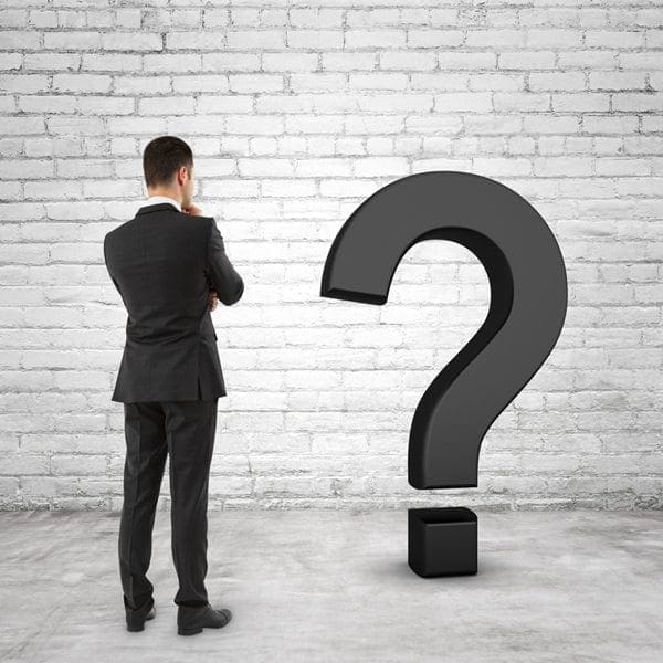 A business professional in a suit studies a bold question mark on a white brick wall, reflecting the realities of cyber risk diligence.